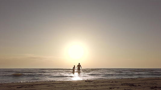 在海滩上一对夫妇握着手在海里跑向相机视频的预览图