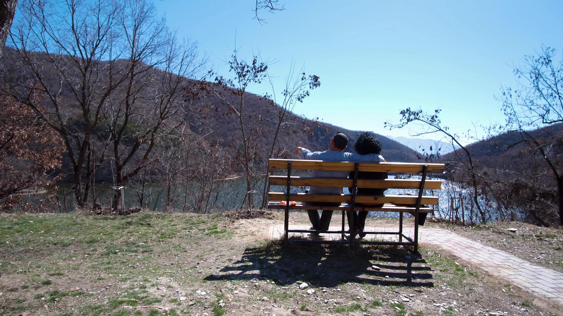 坐在公园的浪漫情侣坐在公园的长椅上看着湖面视频的预览图