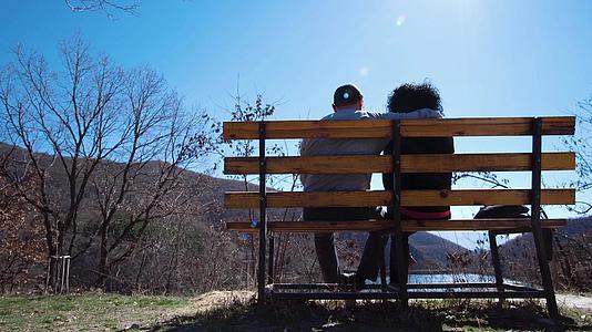 浪漫情侣在山湖边牵手的长椅上视频的预览图