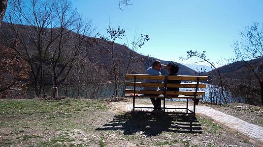 喜欢秋天的年轻夫妇坐在湖前的长凳上视频的预览图
