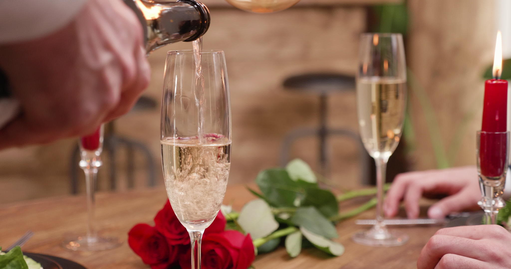 用蜡烛和红玫瑰把香槟倒在桌子上的杯子上视频的预览图