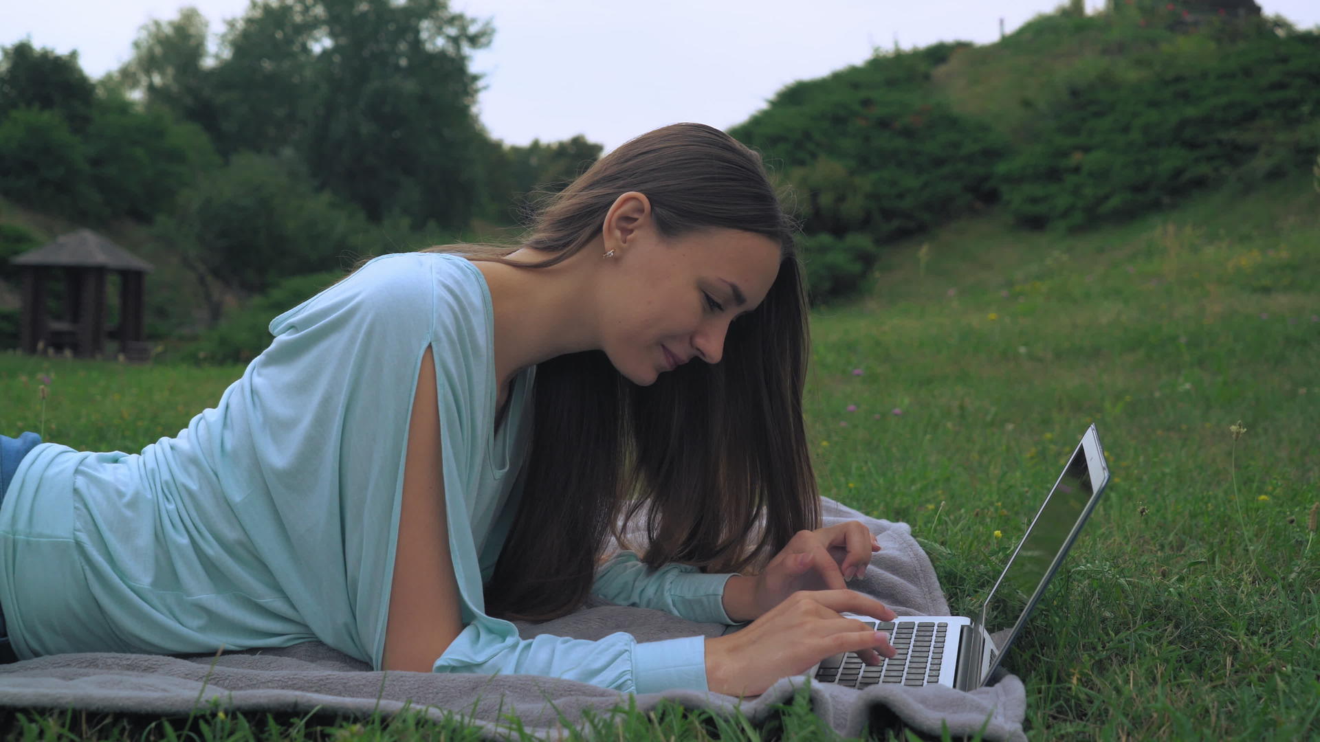 一个年轻女子躺在草坪上在电脑上得到一条信息视频的预览图