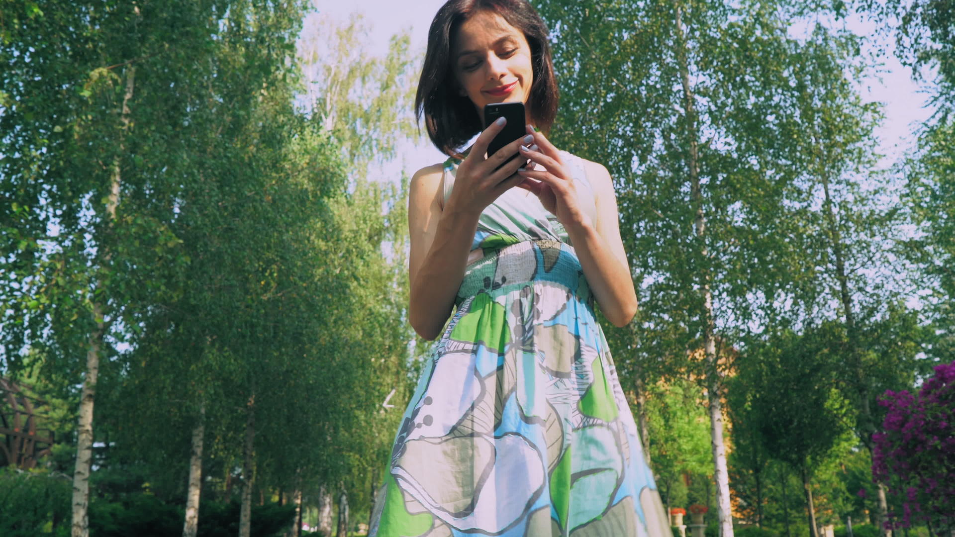 在公园里穿着漂亮裙子的年轻女孩在你的手机上读到信息视频的预览图