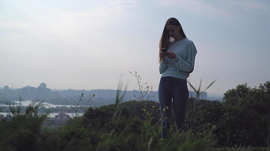 一个年轻的女孩站在山上看着你的手机视频的预览图