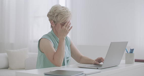 头痛的中年妇女在家用笔记本电脑工作双手触摸前额视频的预览图