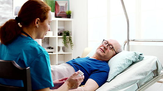 疗养院护理人员向躺在医院床上的男性患者提供处方药视频的预览图