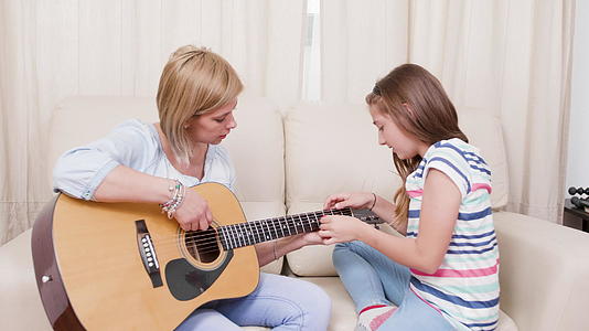 客厅里的母亲和女儿学会了用音响吉他演奏音乐视频的预览图
