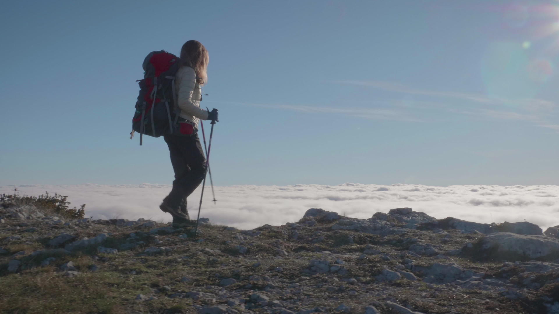 在阳光明媚的日子里背着背包和登山杖的年轻女子在云端视频的预览图