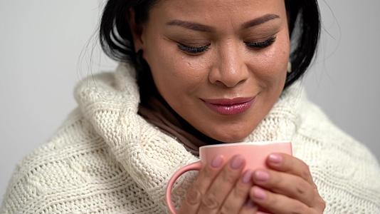 女人甜美的笑容包裹在温暖的围巾里喝着粉色杯里的茶视频的预览图