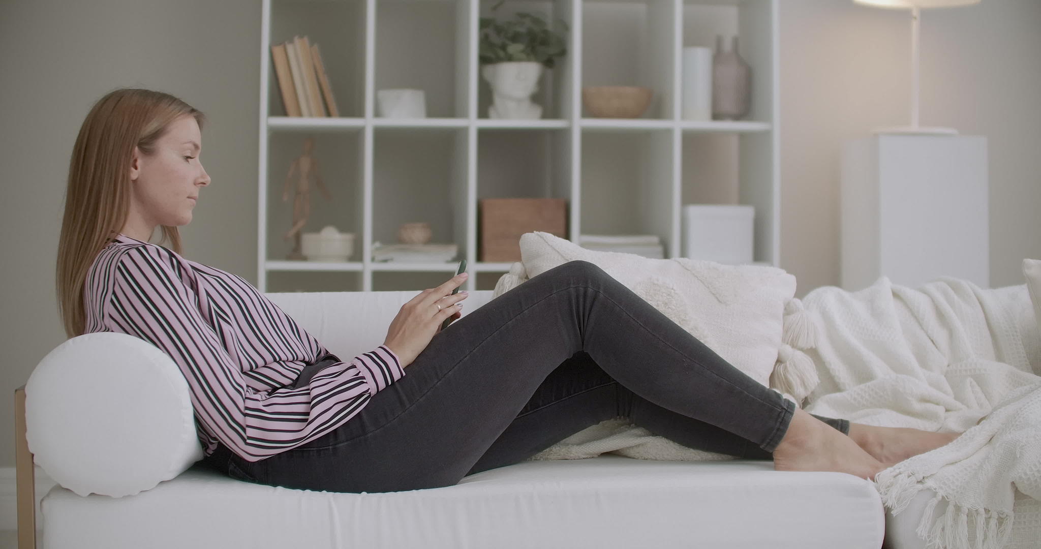 年轻女子在家休息用智能手机聊天睡在客厅的沙发上视频的预览图