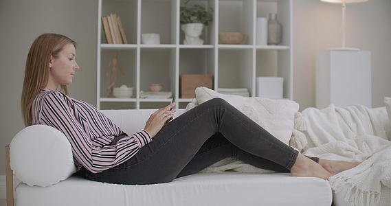 年轻女子在家休息用智能手机聊天睡在客厅的沙发上视频的预览图