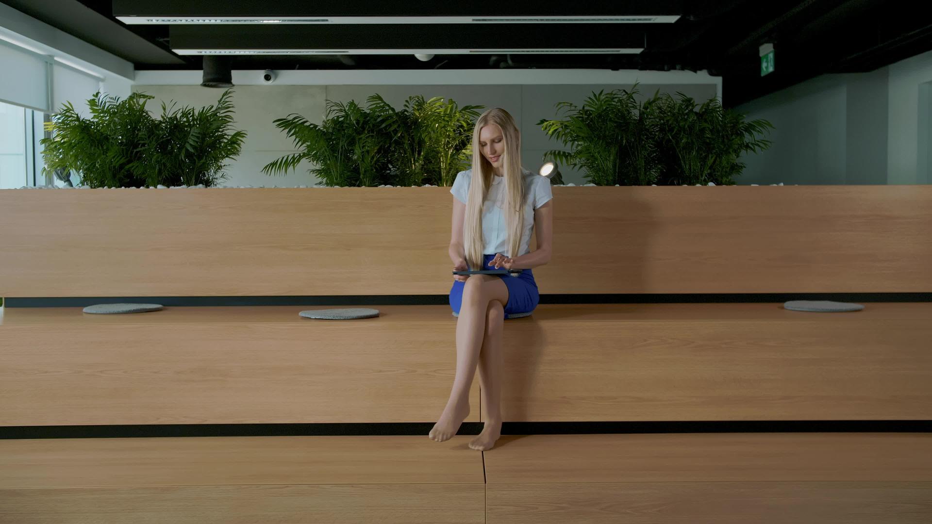 这位年轻优雅的女士赤脚坐在现代办公室的木质法庭上平板电脑视频的预览图