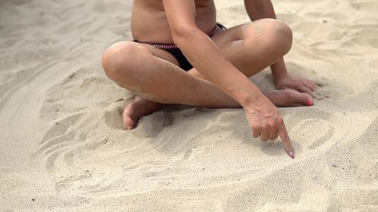 女模特坐在沙滩上用手指慢慢地写信息视频的预览图