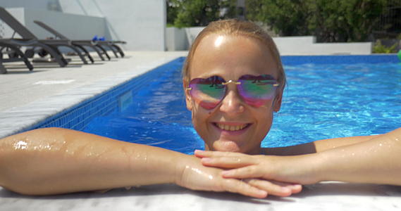 穿着太阳镜的女人在游泳池里享受阳光明媚的一天视频的预览图