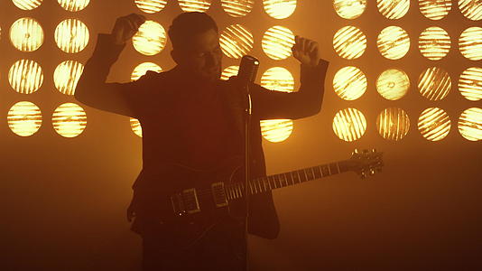 背光下唱歌的专业男吉他手站在舞台上表演歌曲视频的预览图