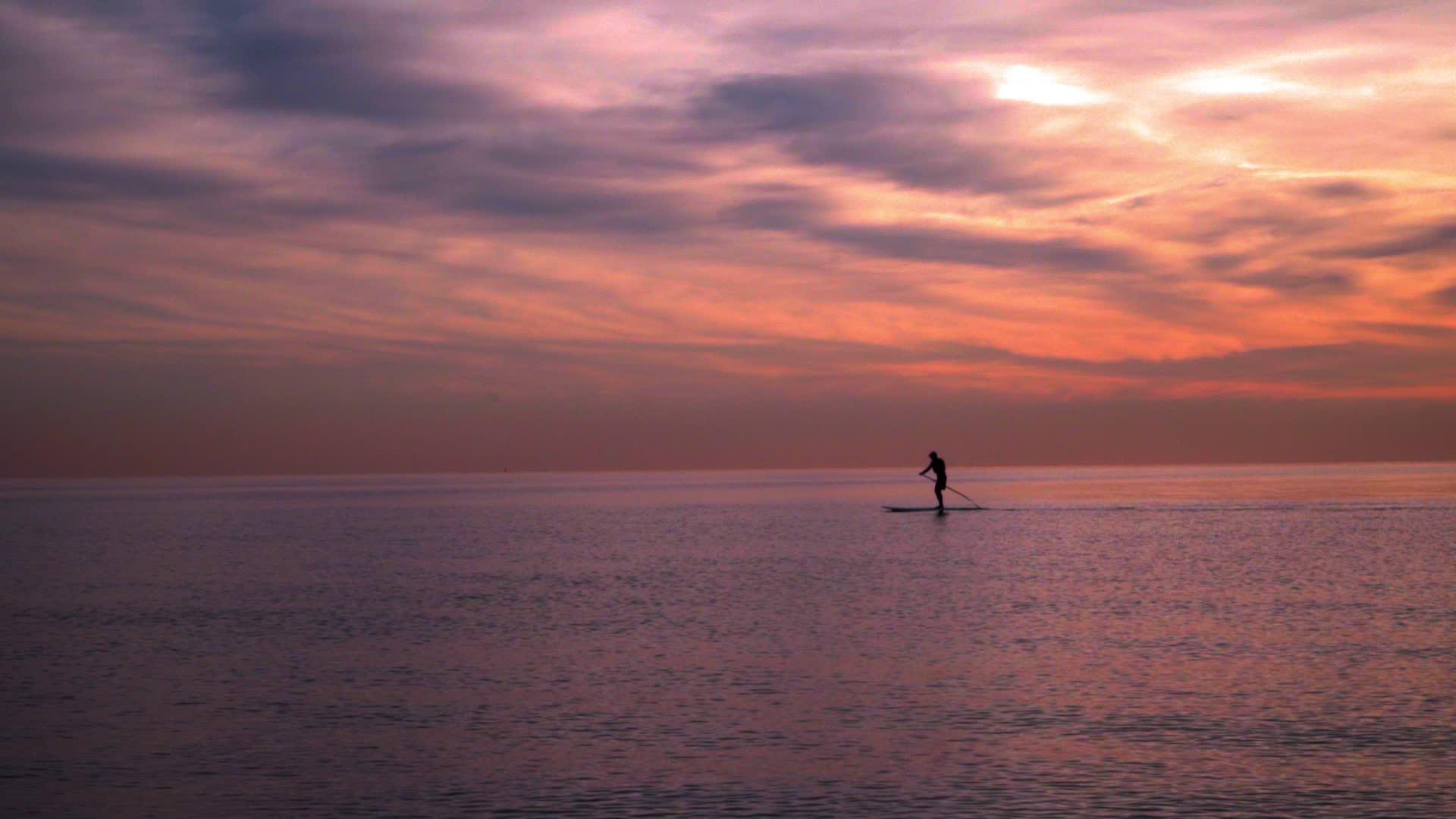 日落时冲浪板上的人海日落景观视频的预览图