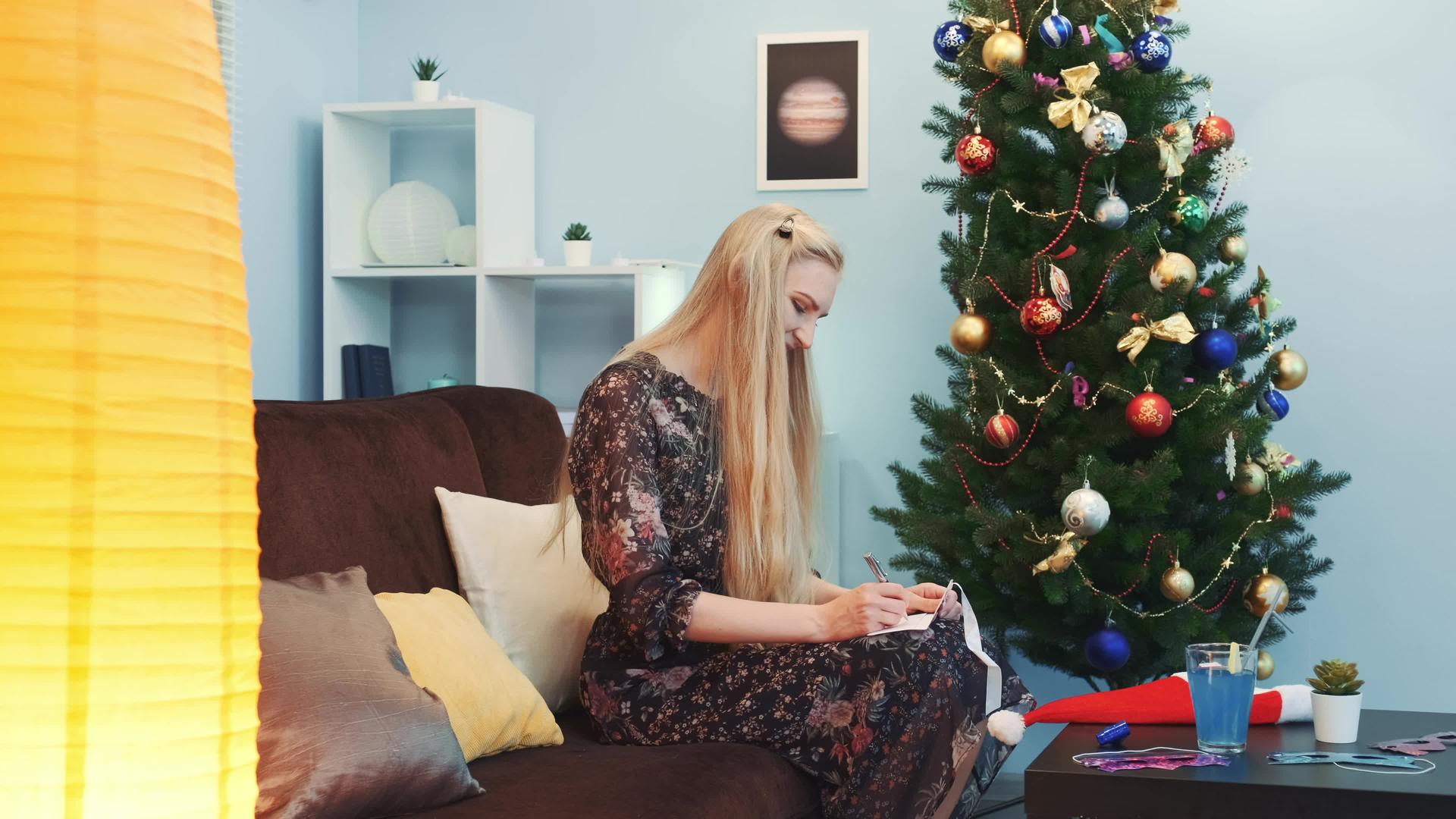 美丽的女人在圣诞树附近写明信片视频的预览图