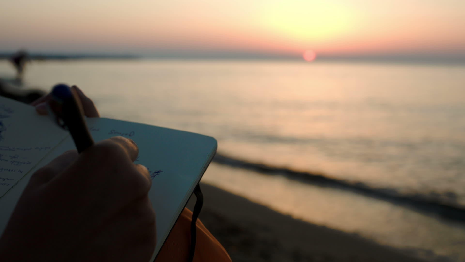 日落时妇女坐在海边做笔记视频的预览图