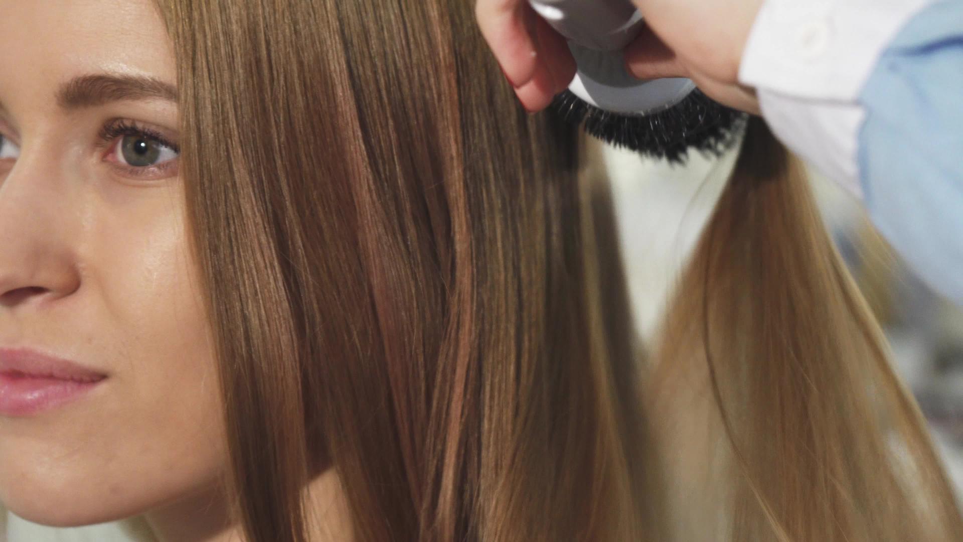 一个漂亮的年轻女子在美发沙龙里梳理她的头发视频的预览图