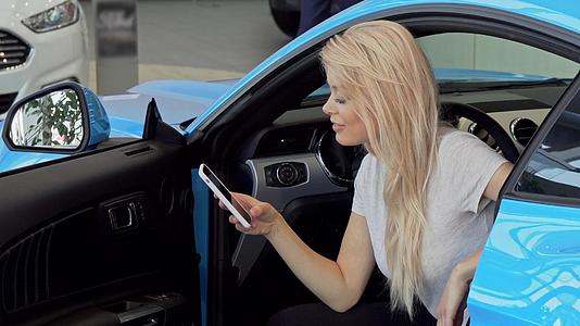 可爱的女士在经销商购买新车时使用智能手机视频的预览图