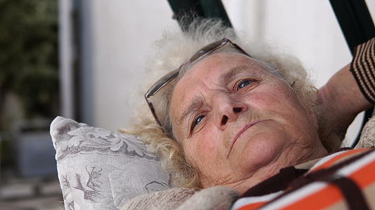 老年妇女躺在门廊的秋千上放松地躺着微笑着躺着视频的预览图