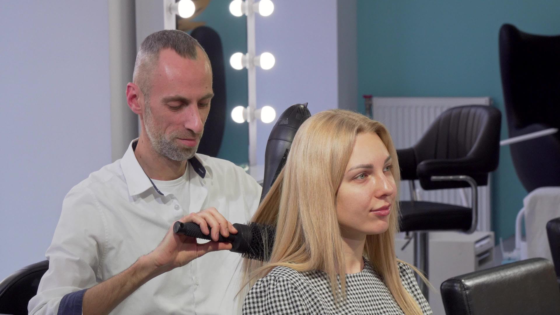 一位成熟的男理发师在沙龙吹了一位女顾客的干发视频的预览图