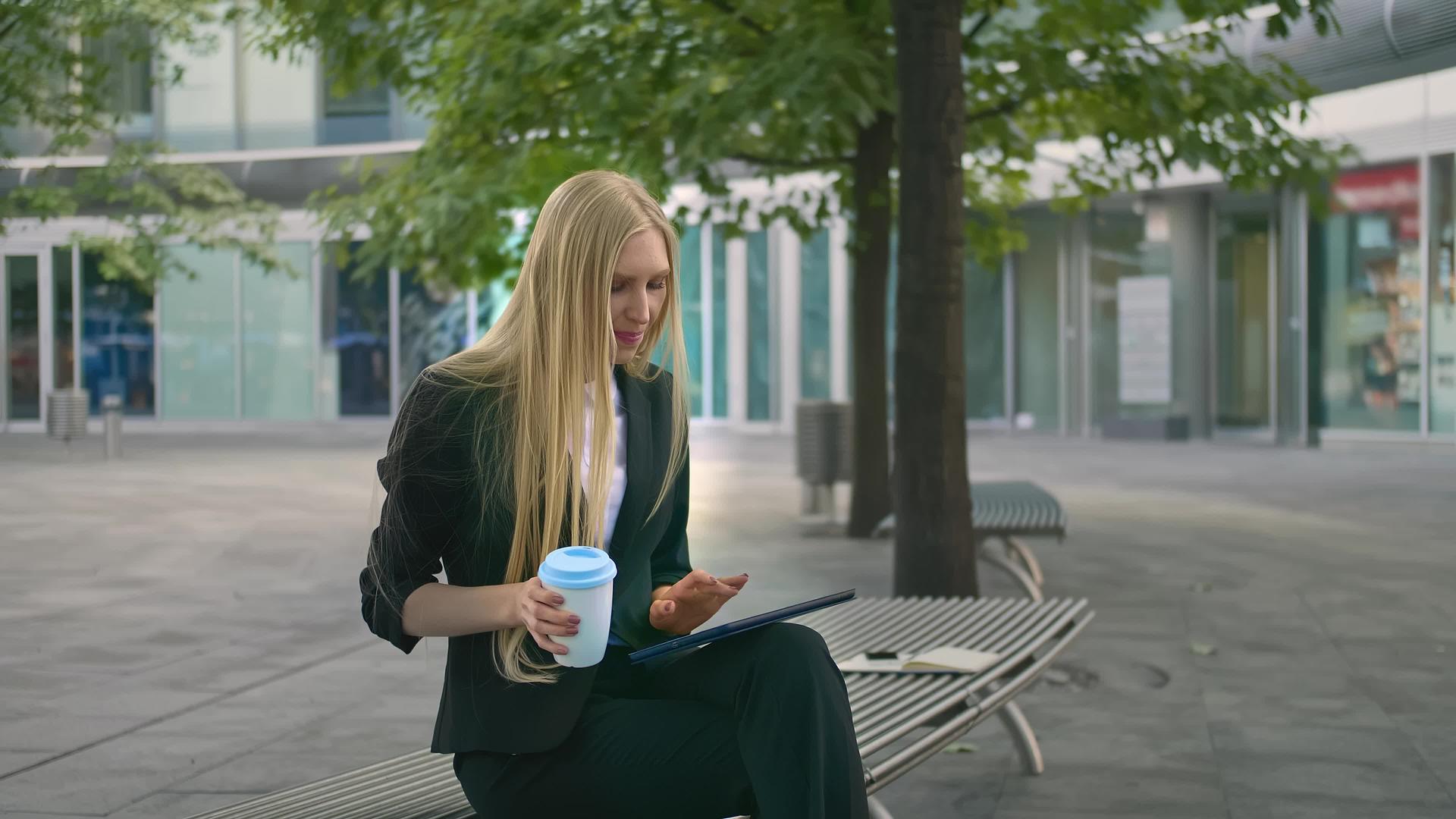穿着西装的现代女执行官坐在户外长椅上冲浪板喝咖啡视频的预览图