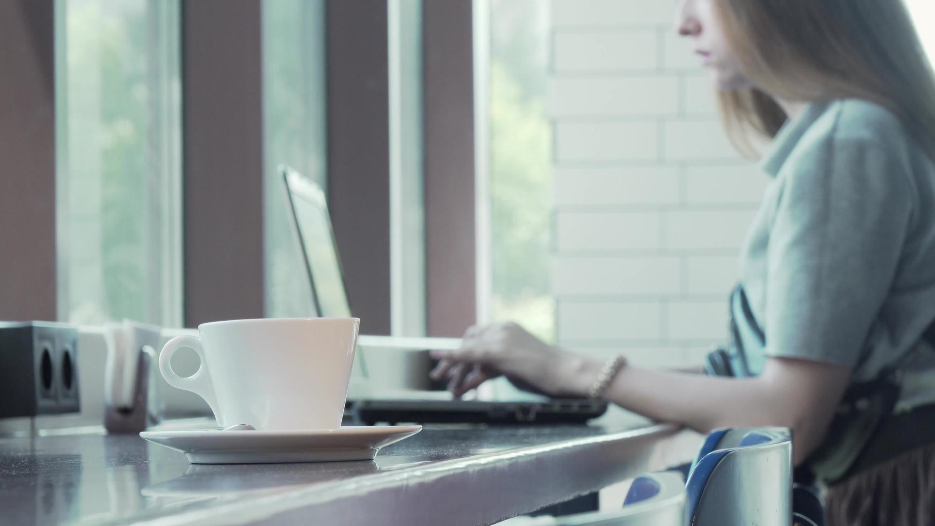 用笔记本电脑做背景工作的女性在桌子上喝咖啡视频的预览图