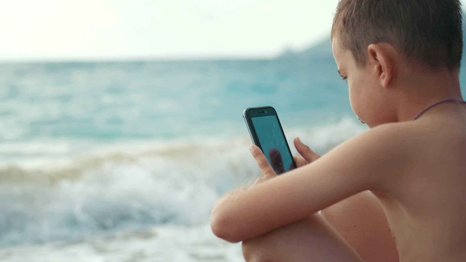 小男孩暑假在海边看手机视频的预览图