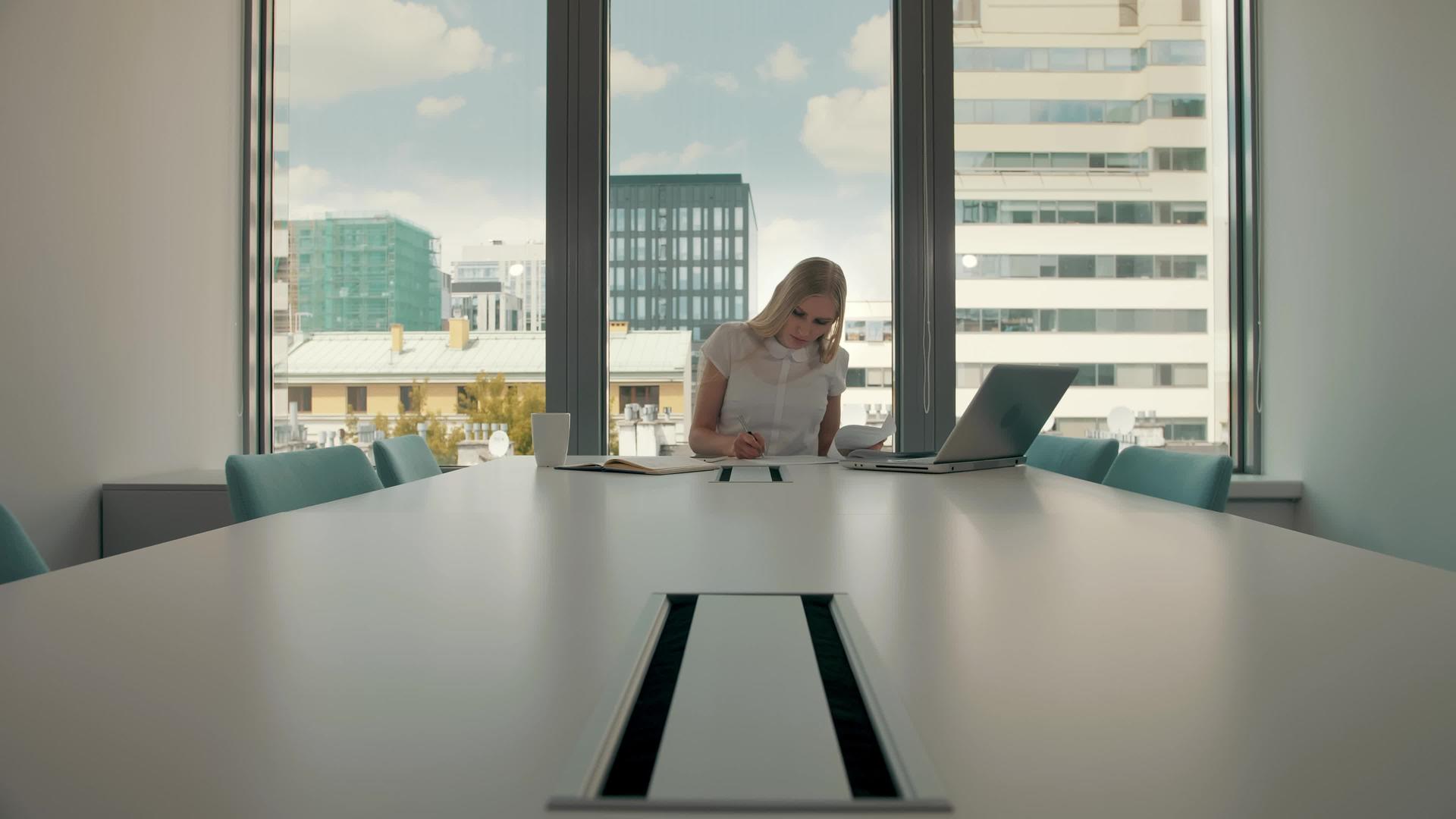 优雅的金发女子坐在现代办公大厅的长桌旁手里拿着笔记本电脑视频的预览图