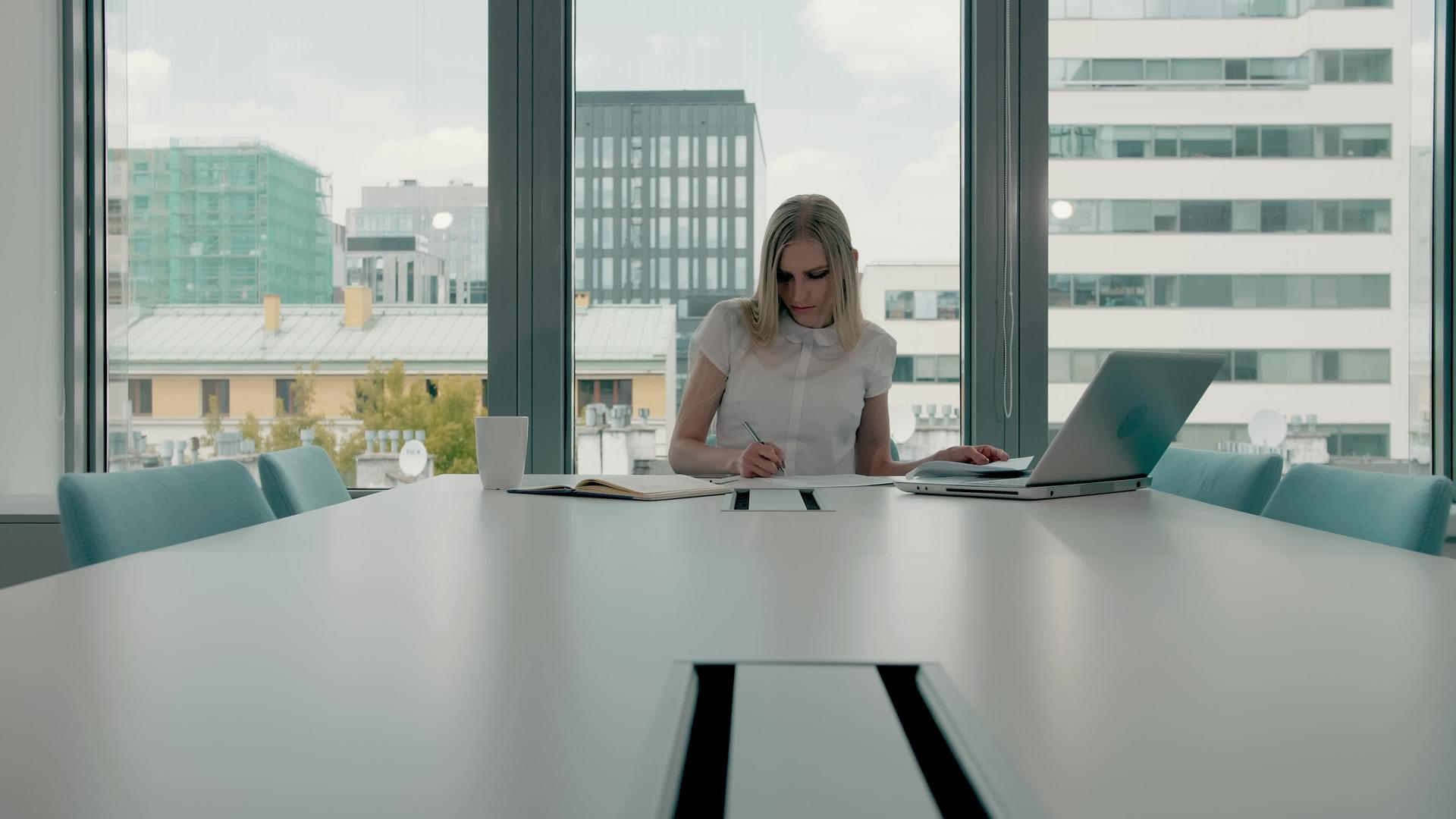 优雅的金发女子坐在现代办公大厅的长桌旁手里拿着笔记本电脑视频的预览图