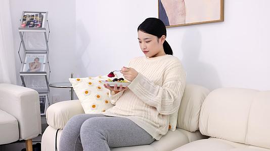 年轻孕妇坐在沙发上吃水果视频的预览图