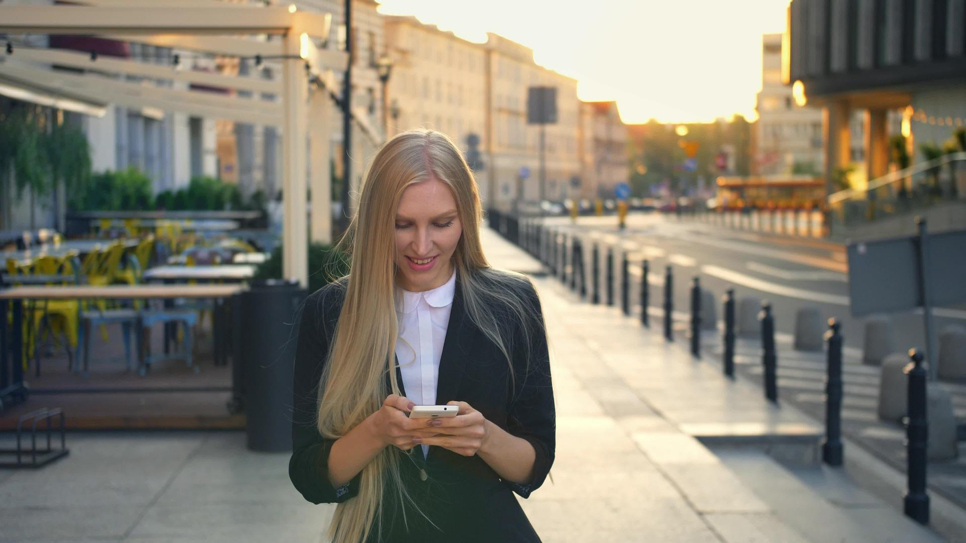 穿着西装的优雅金发女子在街上行走浏览智能手机视频的预览图