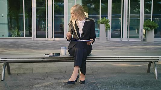 穿着西装的现代商业女性坐在长凳上手里拿着笔记本看不见电话视频的预览图