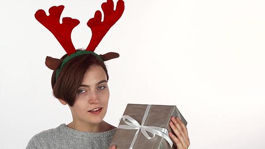 快乐的女人戴着驯鹿鹿角看着她的圣诞礼物视频的预览图