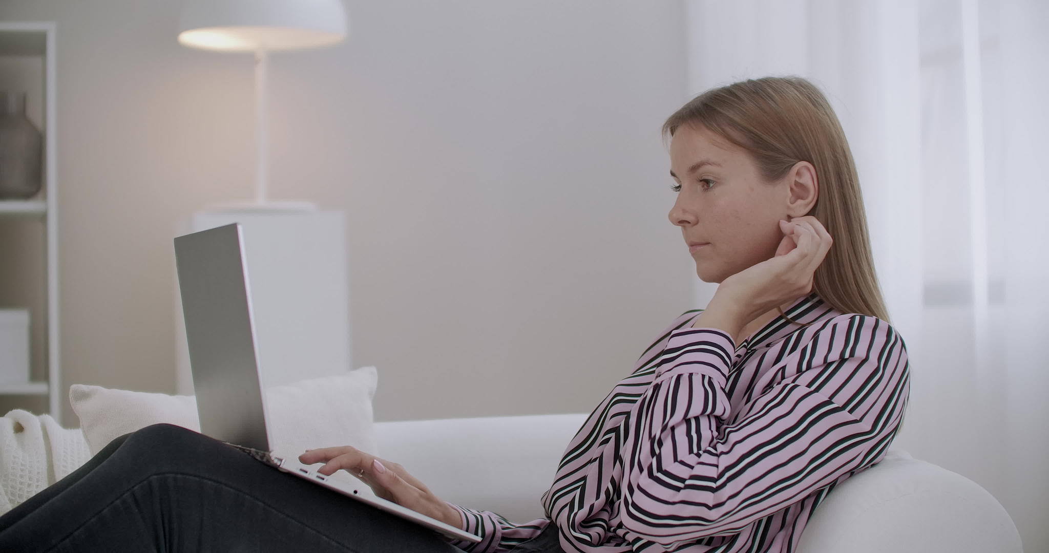 严重的年轻女性在家里用笔记本电脑工作坐在沙发上在社会上工作视频的预览图