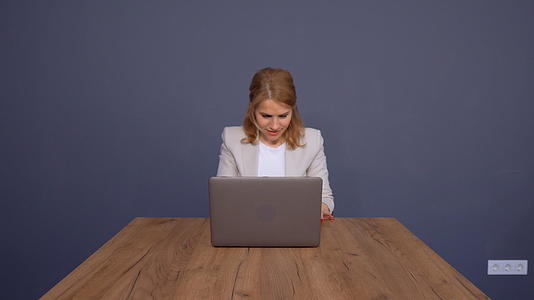 自信的商业女士在蓝色背景的大桌子上做笔记本电脑视频的预览图