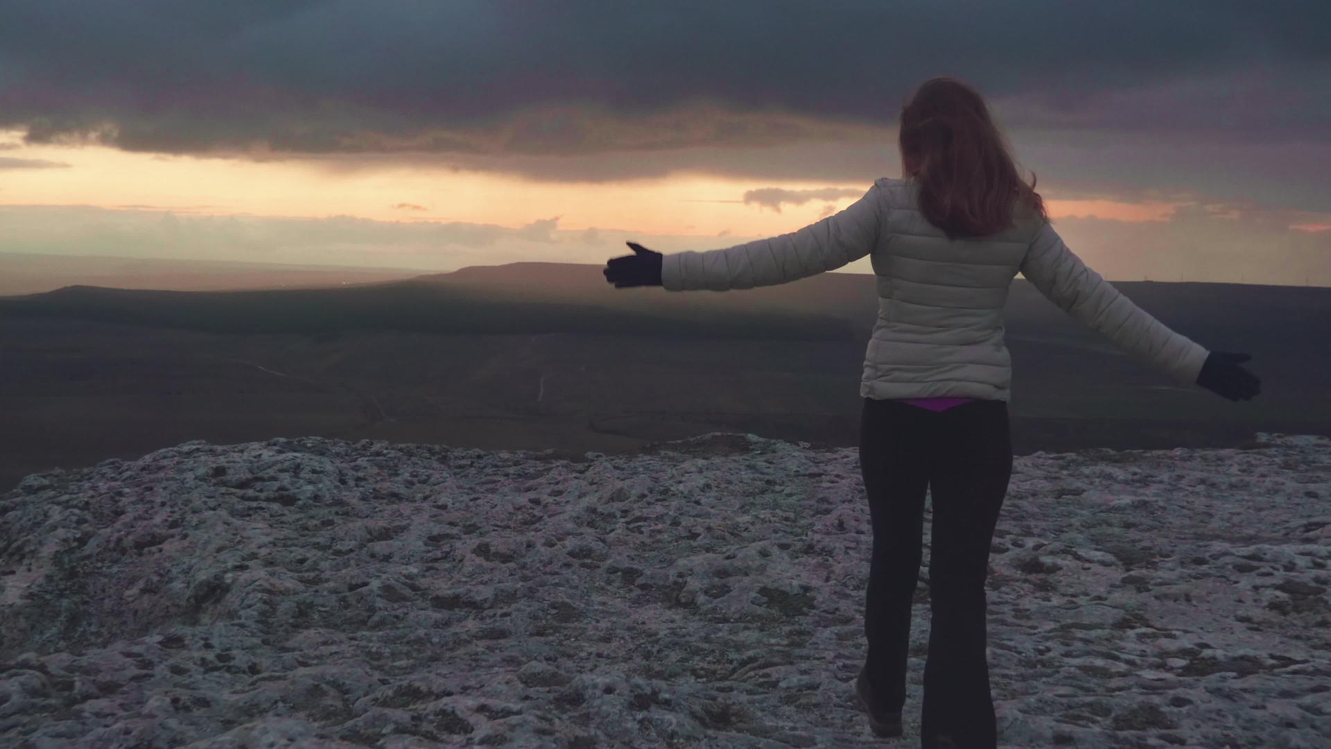 快乐的年轻女子举起手在山顶奔跑吹着头发黄昏时空视频的预览图