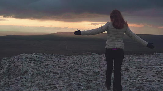 快乐的年轻女子举起手在山顶奔跑吹着头发黄昏时空视频的预览图