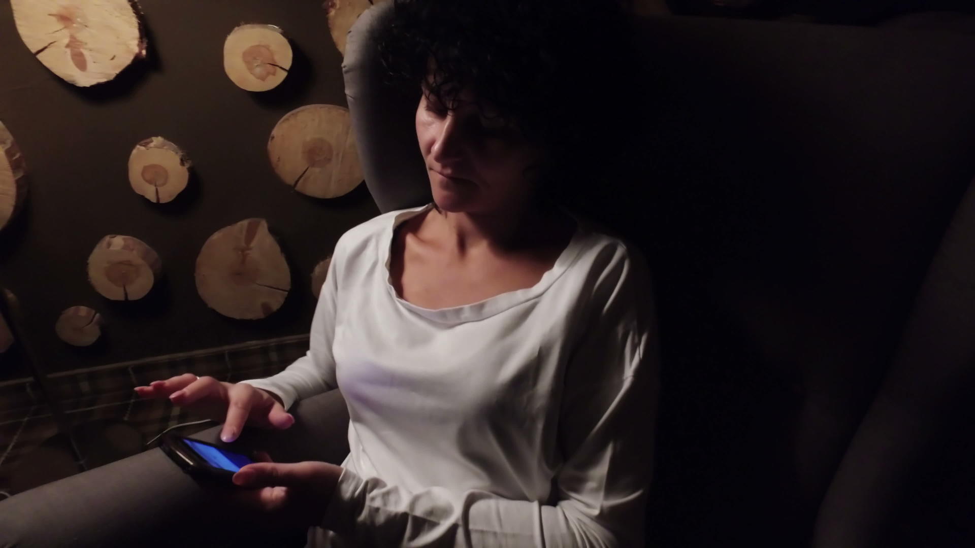 女性晚上使用智能手机坐在灯下扶手椅上放松视频的预览图