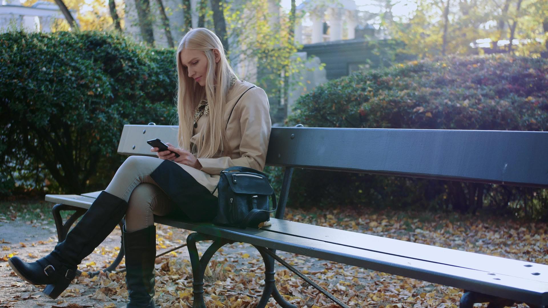 秋天公园里穿着时髦夹克的漂亮女孩在阳光明媚的公园里使用视频的预览图