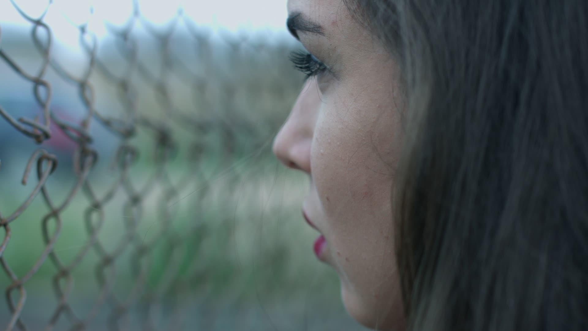 一个脸上有黑发的年轻女子透过栅栏网侧视视频的预览图