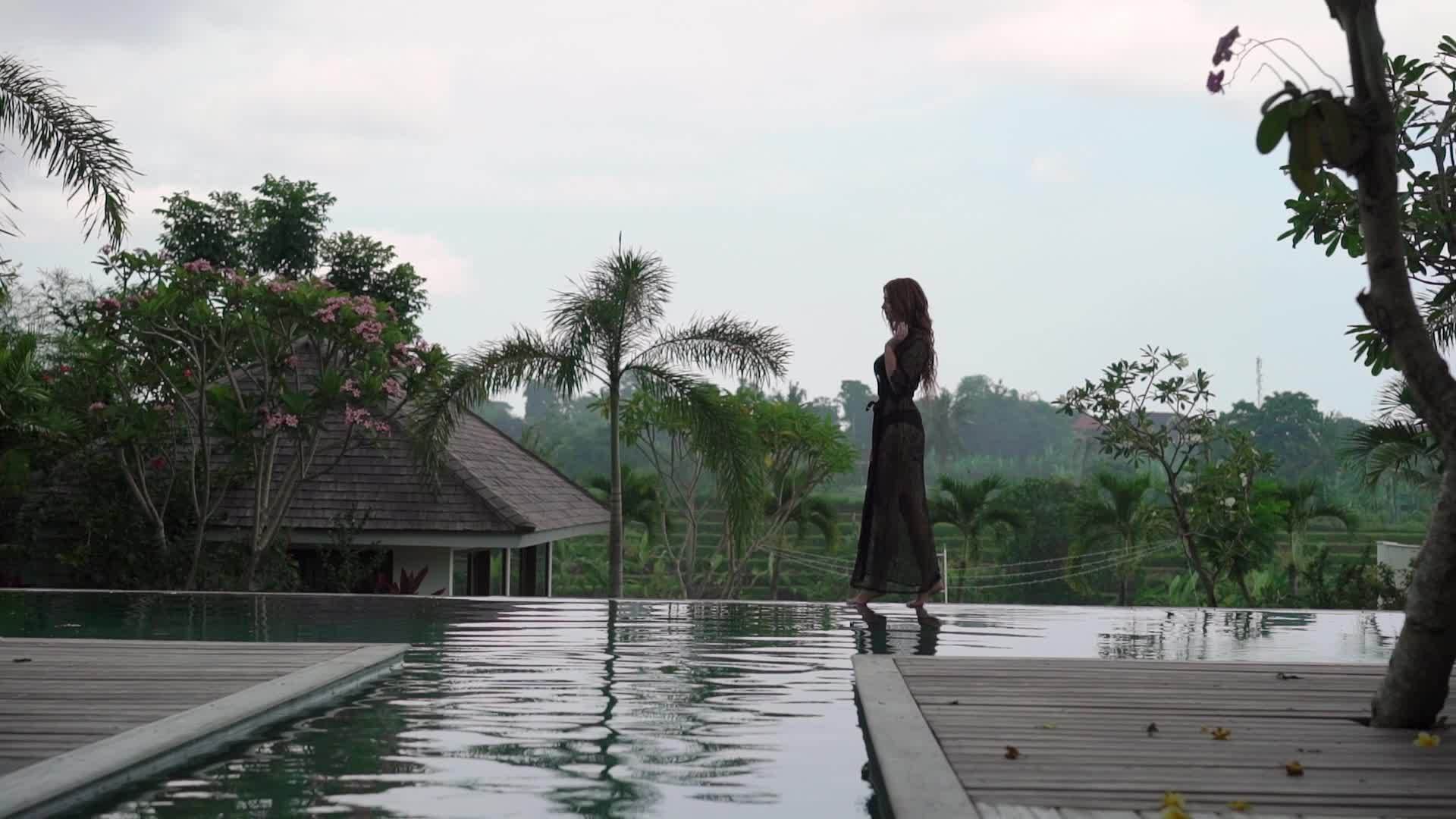 穿着黑色内衣的年轻性感女性走在豪华别墅游泳池附近视频的预览图