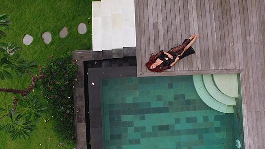 年轻性感的女人穿着黑色内衣躺在豪华别墅游泳池附近视频的预览图