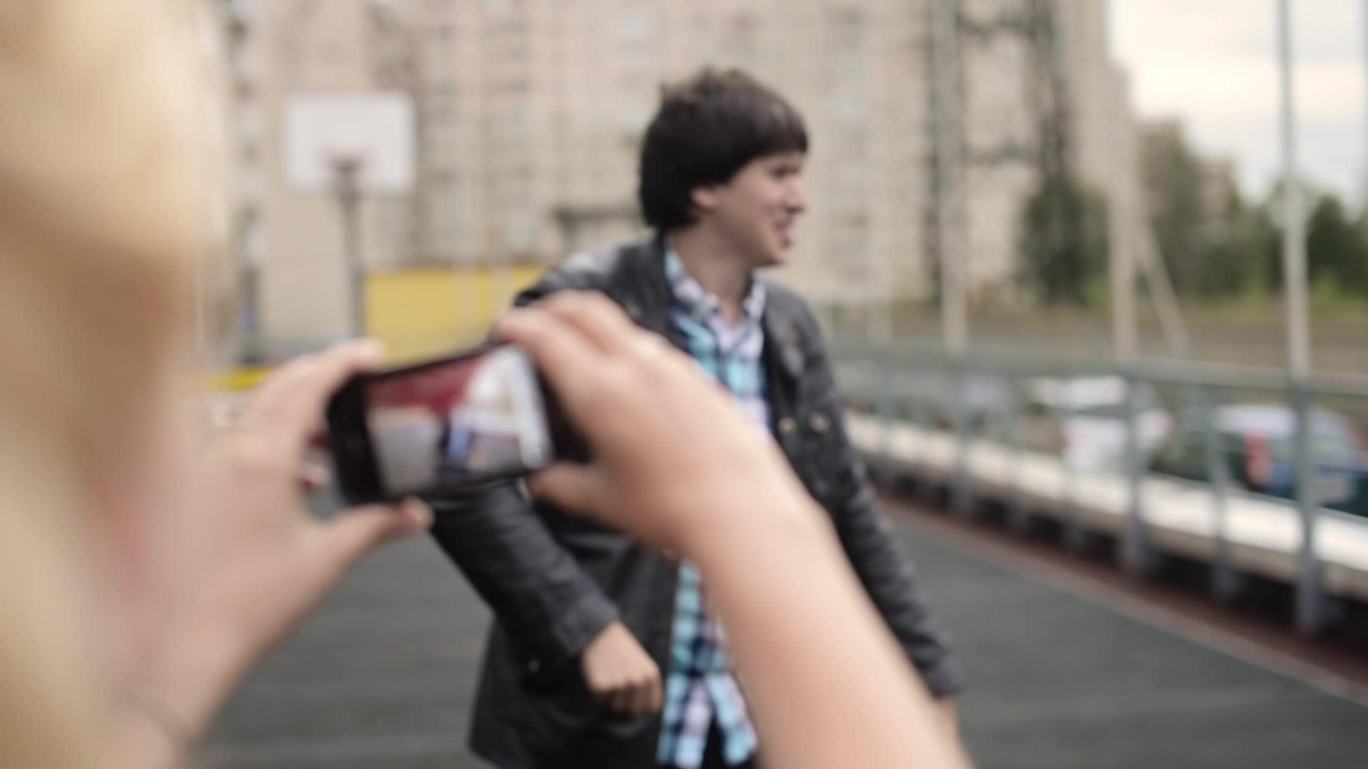 年轻女孩用手机拍摄男友在街上玩耍的男友的照片视频的预览图