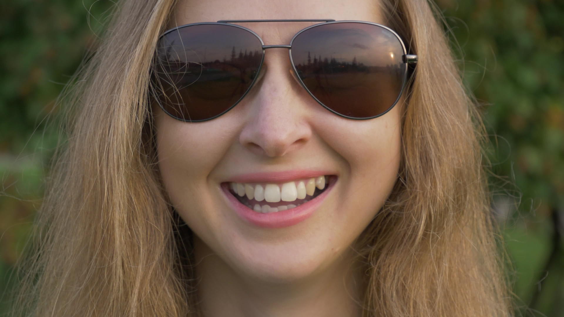 穿着太阳镜的白人年轻女子在公园里微笑近距离拍摄视频的预览图