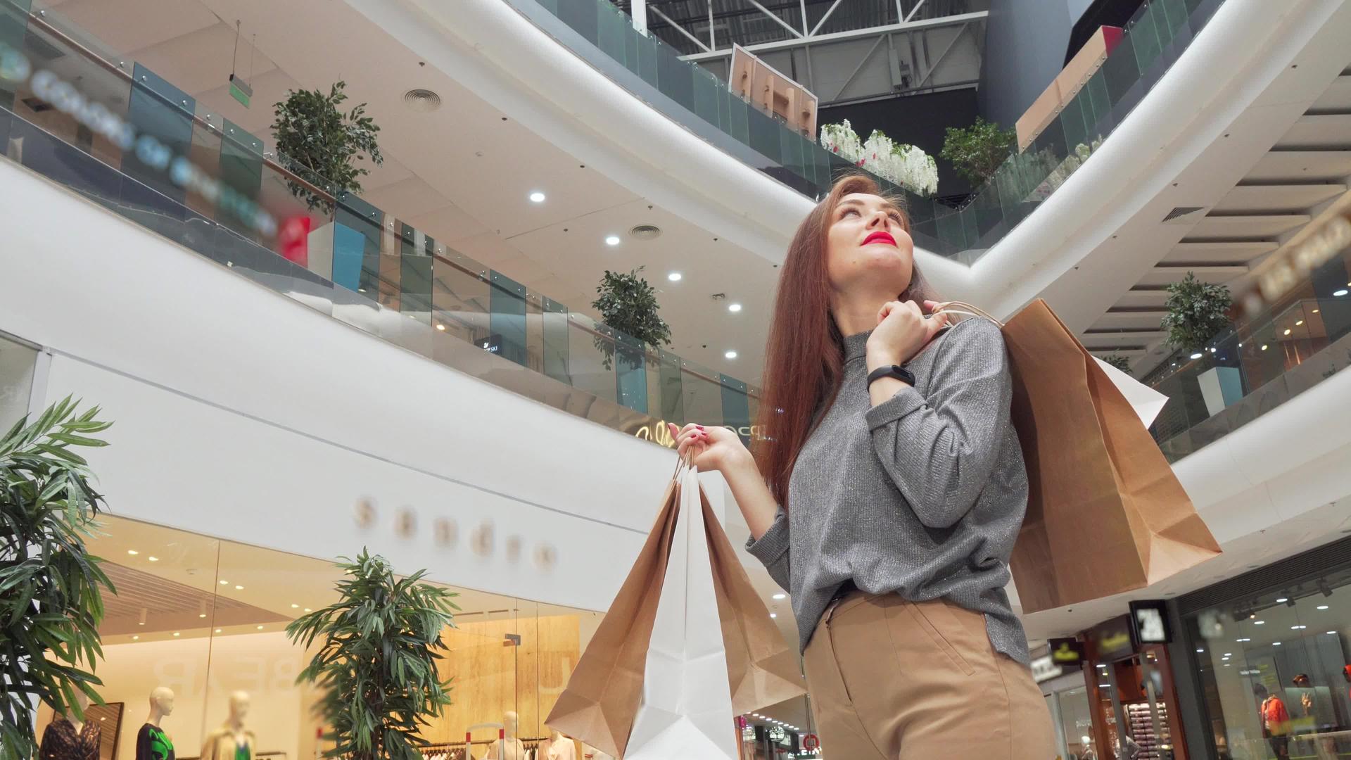 一个带着购物袋的快乐女人看着商场周围的低角度拍摄视频的预览图