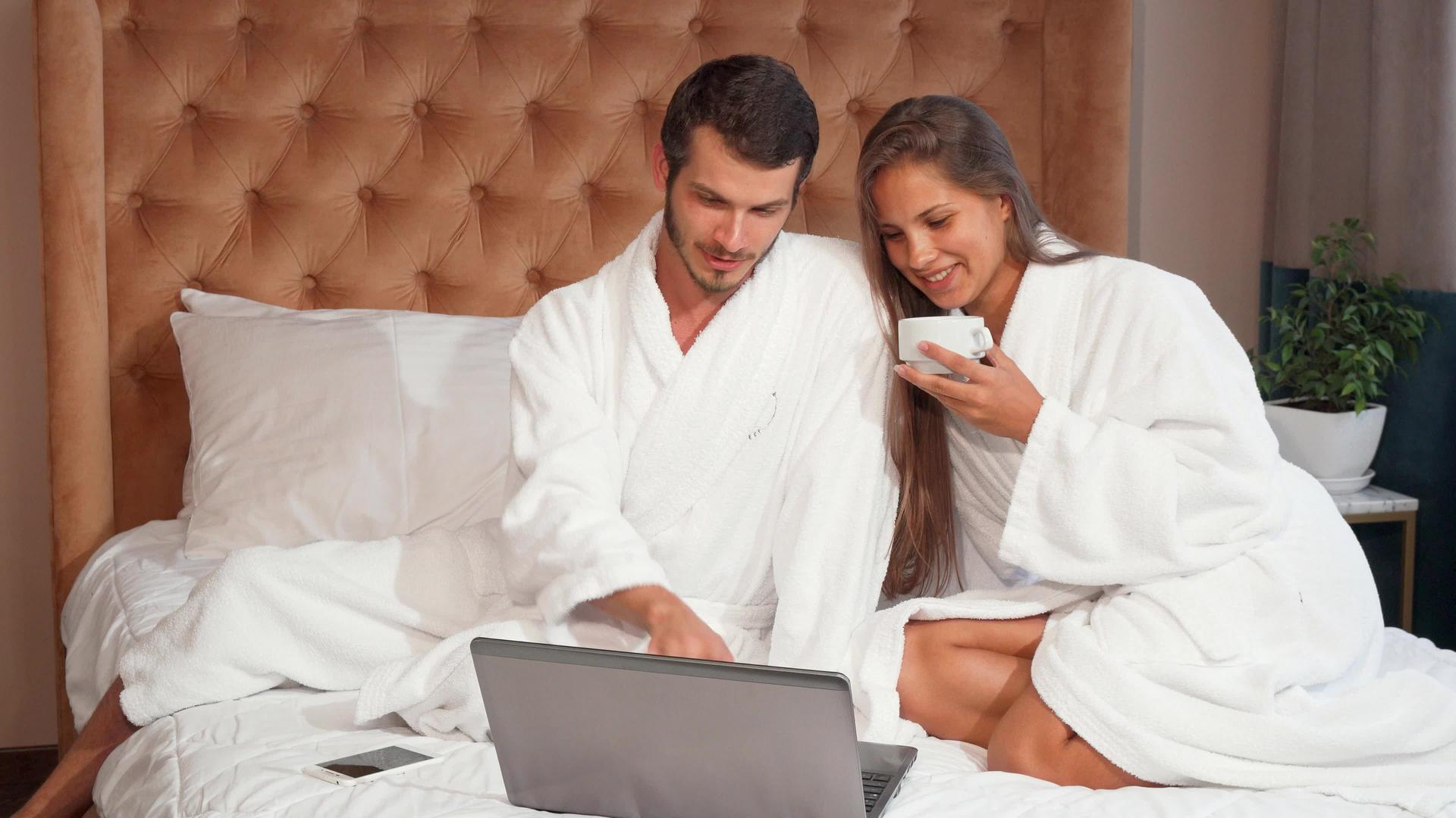 年轻夫妇在床上喝咖啡时使用笔记本电脑视频的预览图