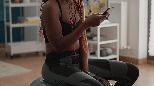 黑人健康女性穿着运动服坐在瑜伽瑞士球上视频的预览图