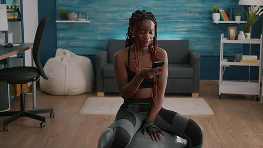 穿着运动服的黑皮肤坐在瑜伽双体球上的女性视频的预览图